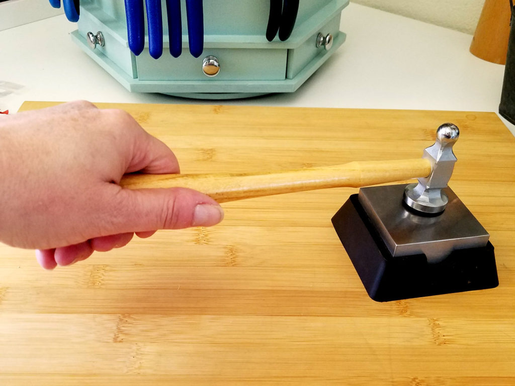 This image illustrates the correct hand position in reference to the bench block. The handle of the chasing hammer should be roughly parallel to the surface of the bench block. 