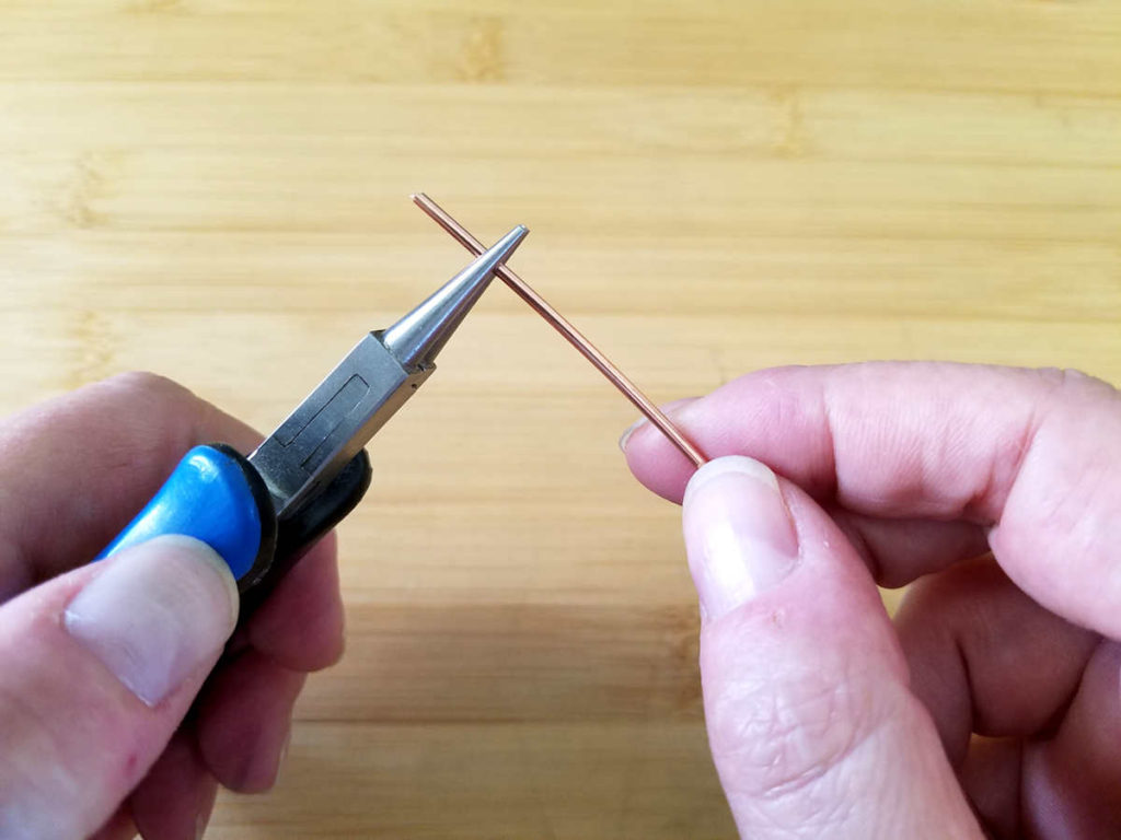 In this image, the author is grasping the end of a piece of 14ga wire with round nose pliers and squeezing the wire, as instructed in the exercise. 