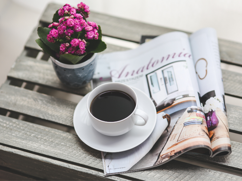 A cup of coffee on a table with flowers and a magazine
