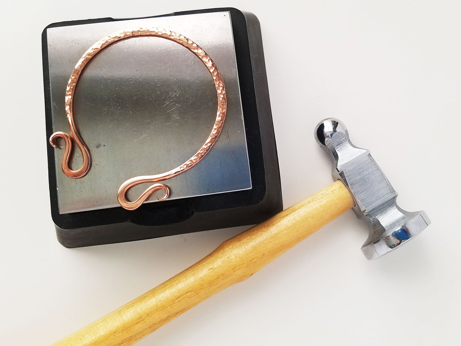 A chasing hammer and a bench block with a piece of hammered copper wire